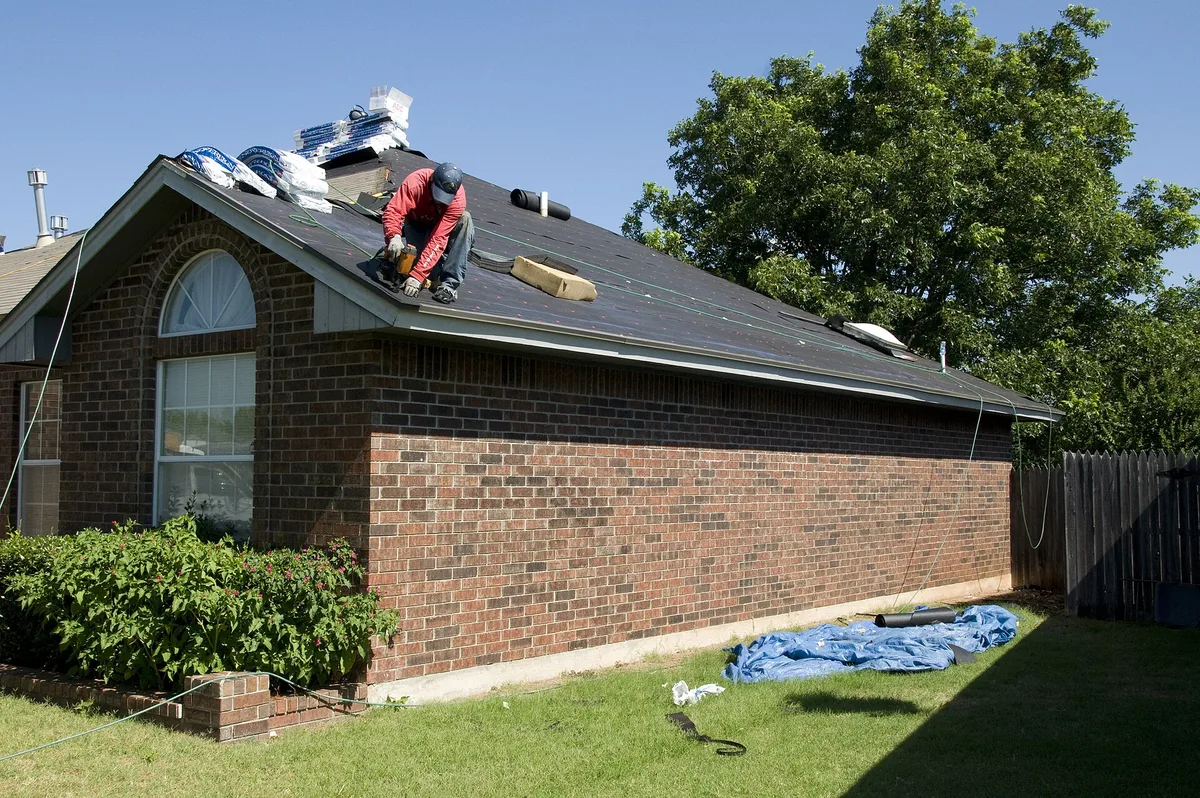 A roofer fastening shingles on a residential roof